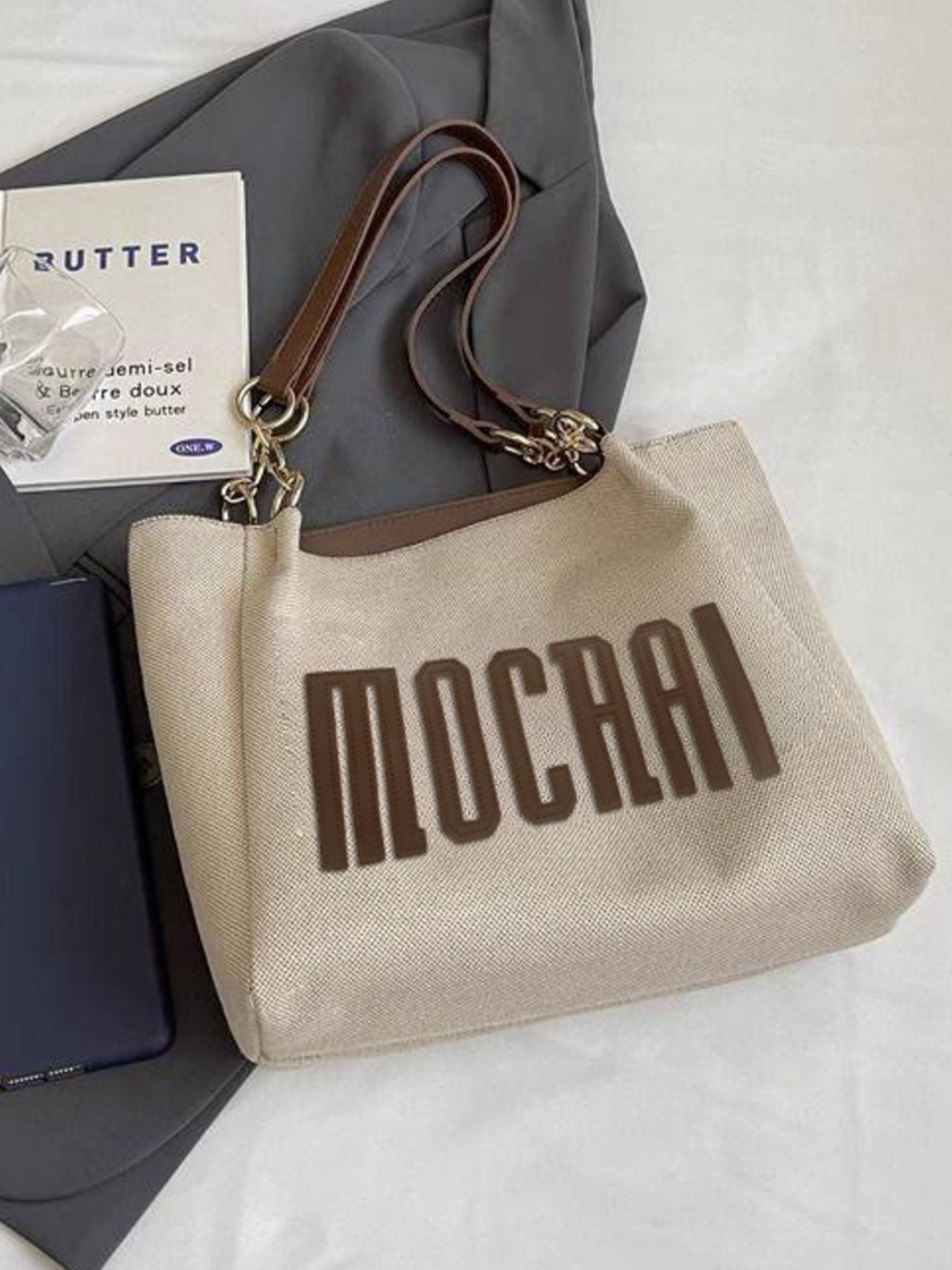 Textured canvas shoulder bag in brown with chain accents and "MOCHAI" lettering.