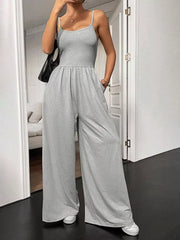 Grey wide-leg maternity romper with spaghetti straps and elastic waist, styled with sneakers.