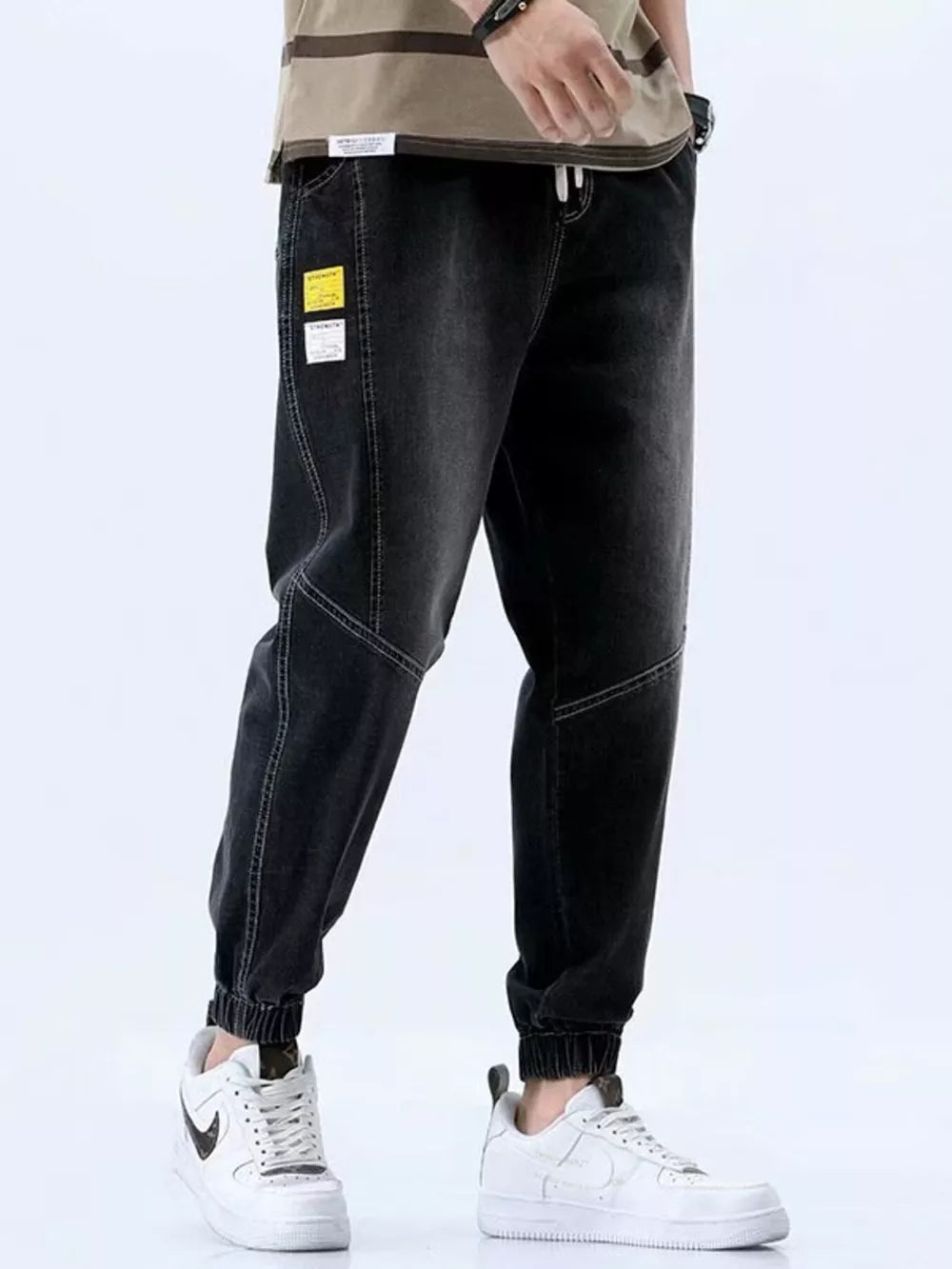 Men's black relaxed fit drawstring jeans with elastic cuffs and contrast stitching.