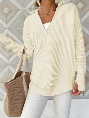 Cream ribbed knit funnel neck pullover with quarter zip and thumbholes, styled with white pants and a tote bag.