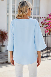 Light blue blouse with asymmetric bell sleeves and a curved hem.