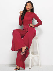 Red high-waisted palazzo jumpsuit with slit front and long sleeves.