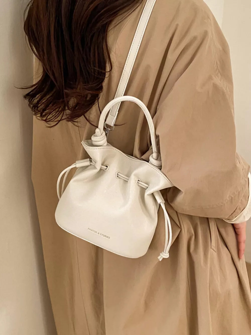 White pu leather cinch-top crossbody bag with drawstring closure and top handle.