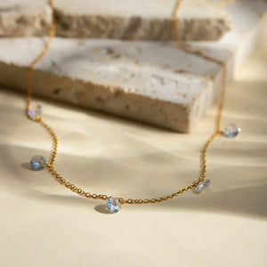 Gold dangling crystal station necklace with a delicate chain and scattered blue crystals.