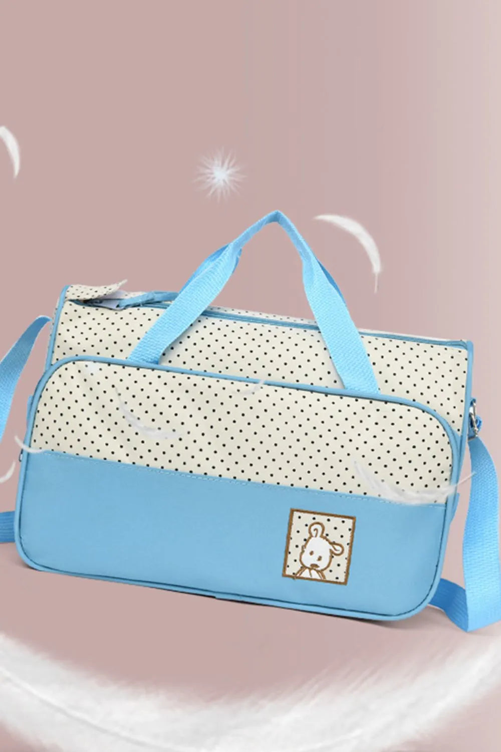 Pastel blue and white polka dot diaper bag with embroidered bear detail and blue straps.