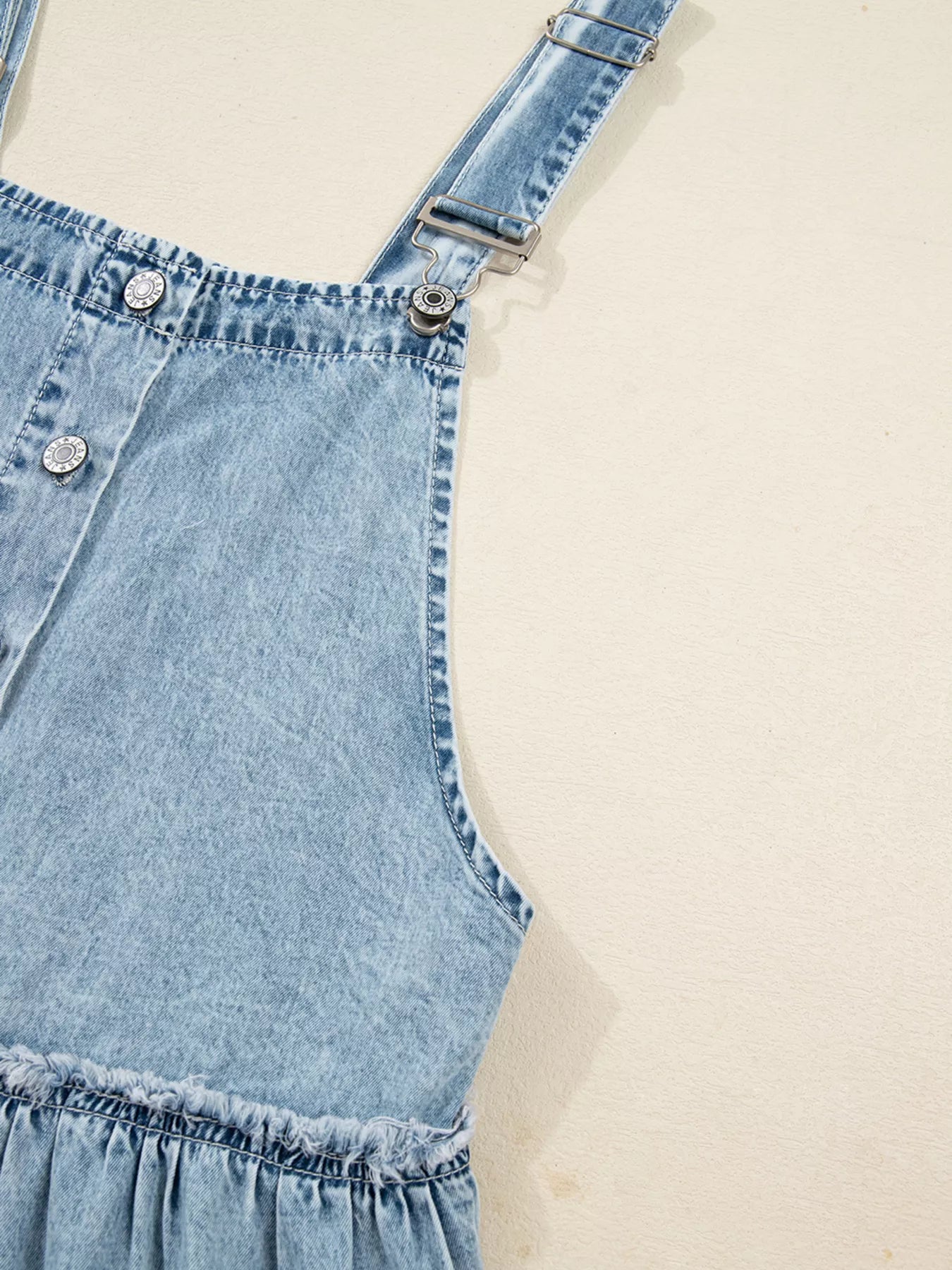 Light blue denim tiered overall dress with button front and ruffled hem detail.