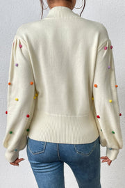 Cream blouson knit sweater with colorful pom-pom embellishments on sleeves.