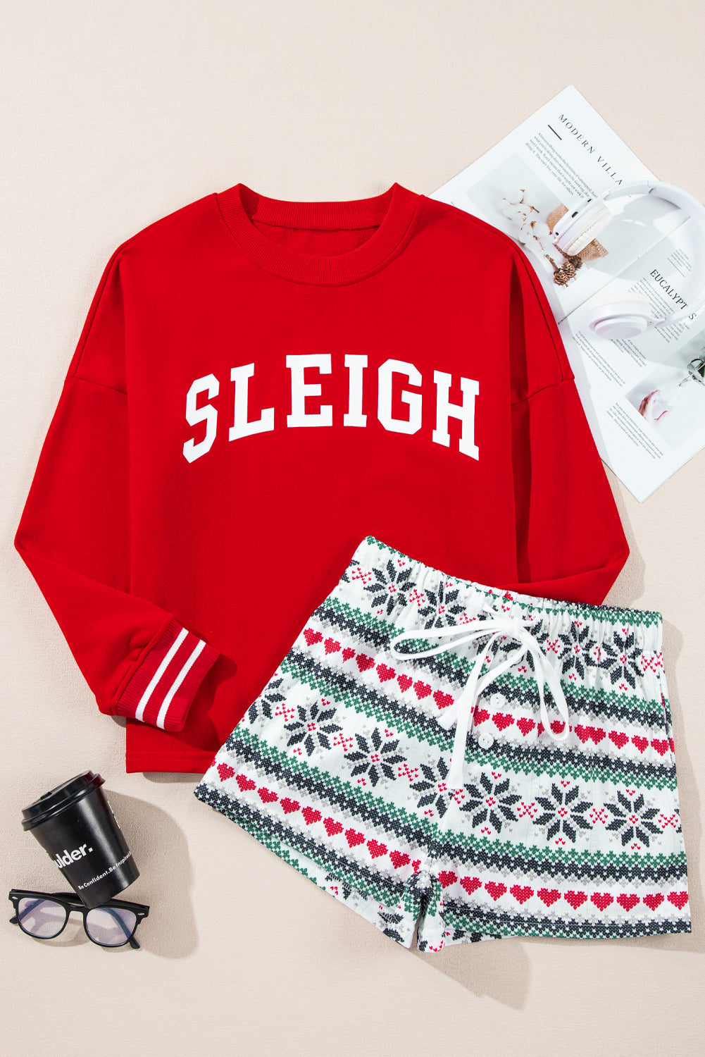 Red crewneck sweatshirt with "Sleigh" graphic and patterned shorts with hearts and snowflakes.
