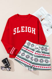 Red crewneck sweatshirt with "Sleigh" graphic and patterned shorts with hearts and snowflakes.