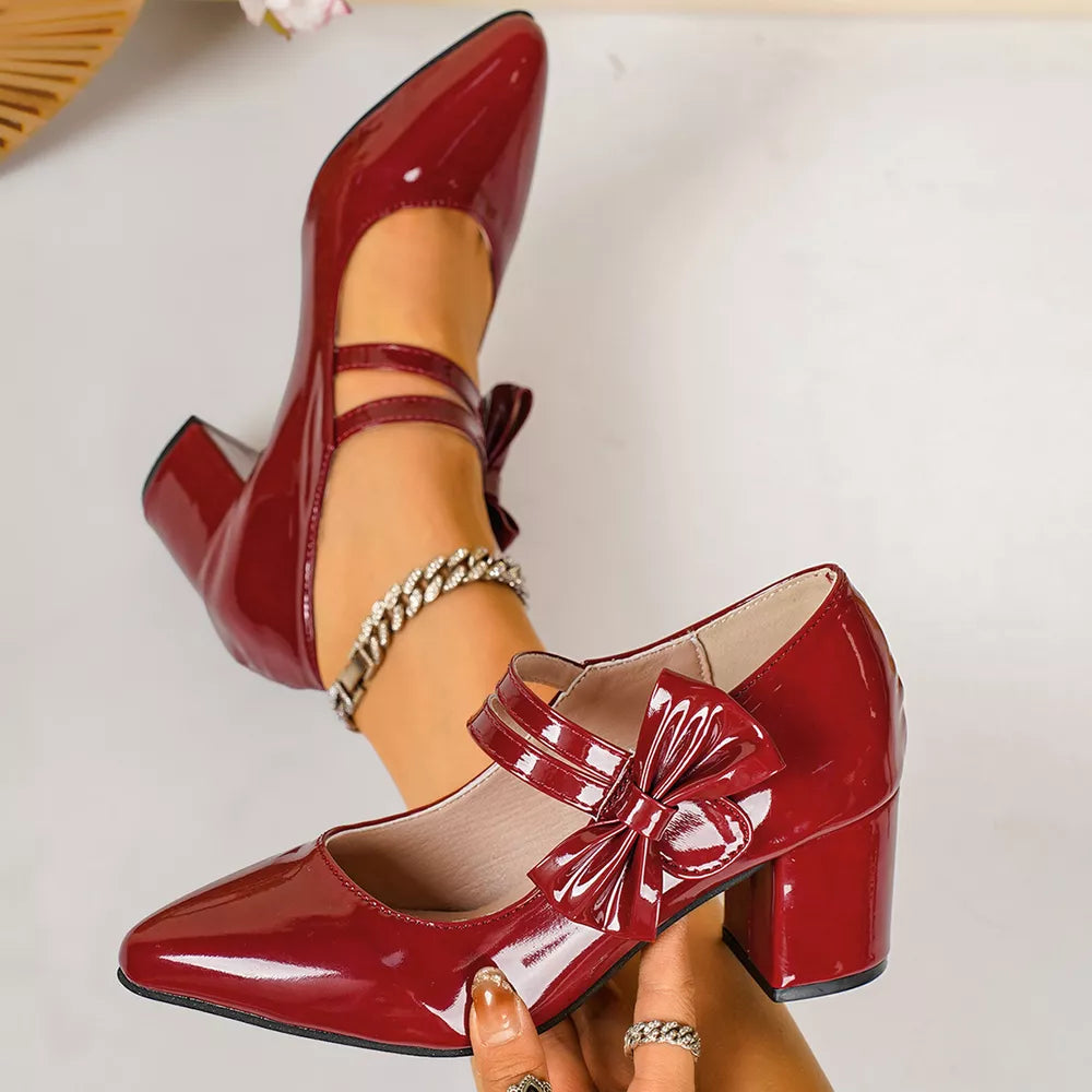 Red patent block heel pumps with pointed toe and double ankle straps with bow detail.