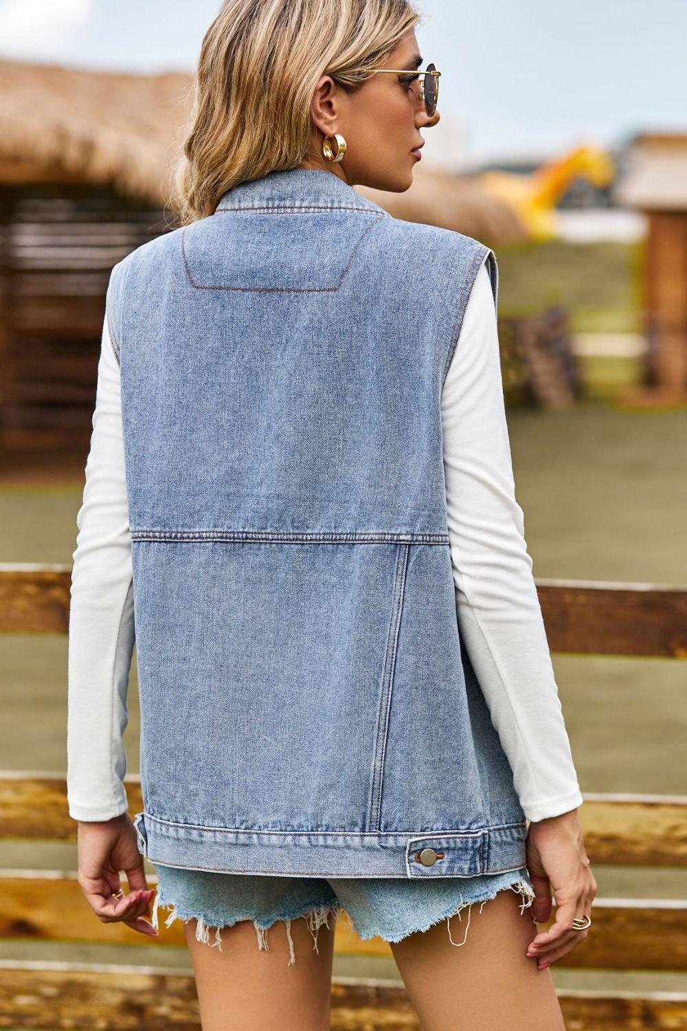 Sleeveless light wash denim utility vest with button details and a classic collar.