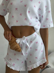White knit lounge set with pink bow print, cropped top, and ruffled shorts with drawstring.