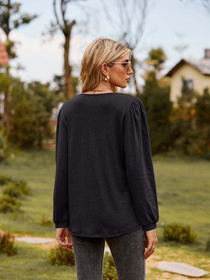 Black ruffled henley sleeve blouse with gathered shoulders and cinched cuffs.