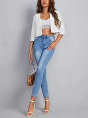 White cropped open-front blazer with elbow sleeves and a relaxed fit, styled with jeans.