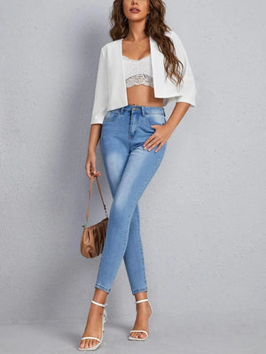 White cropped open-front blazer with elbow sleeves and a relaxed fit, styled with jeans.
