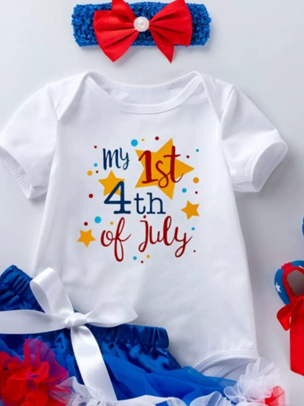 White baby onesie with "my 1st 4th of July" text and stars, paired with blue bloomer and red bow headband.