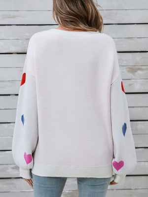 White knit sweater with bubble sleeves and scattered heart motif in pink, red, and blue.