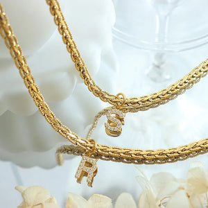 Gold textured chain necklace with initial charms R and S, detailed with rhinestones.