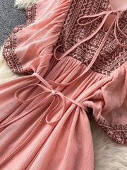 Pink V-neck maxi dress with embroidered yoke and sleeves, tie waist, and textured fabric.