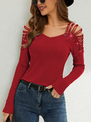 Red ribbed knit blouse with cold shoulder cutouts and sparkling embellishments on the sleeves.