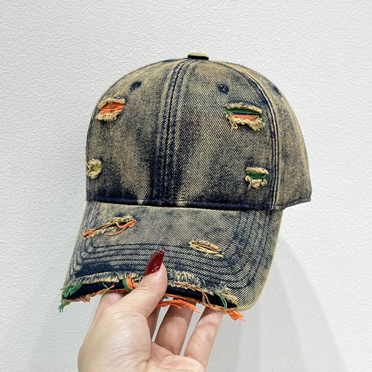 Distressed denim baseball cap with fraying and colorful threads showing through holes.