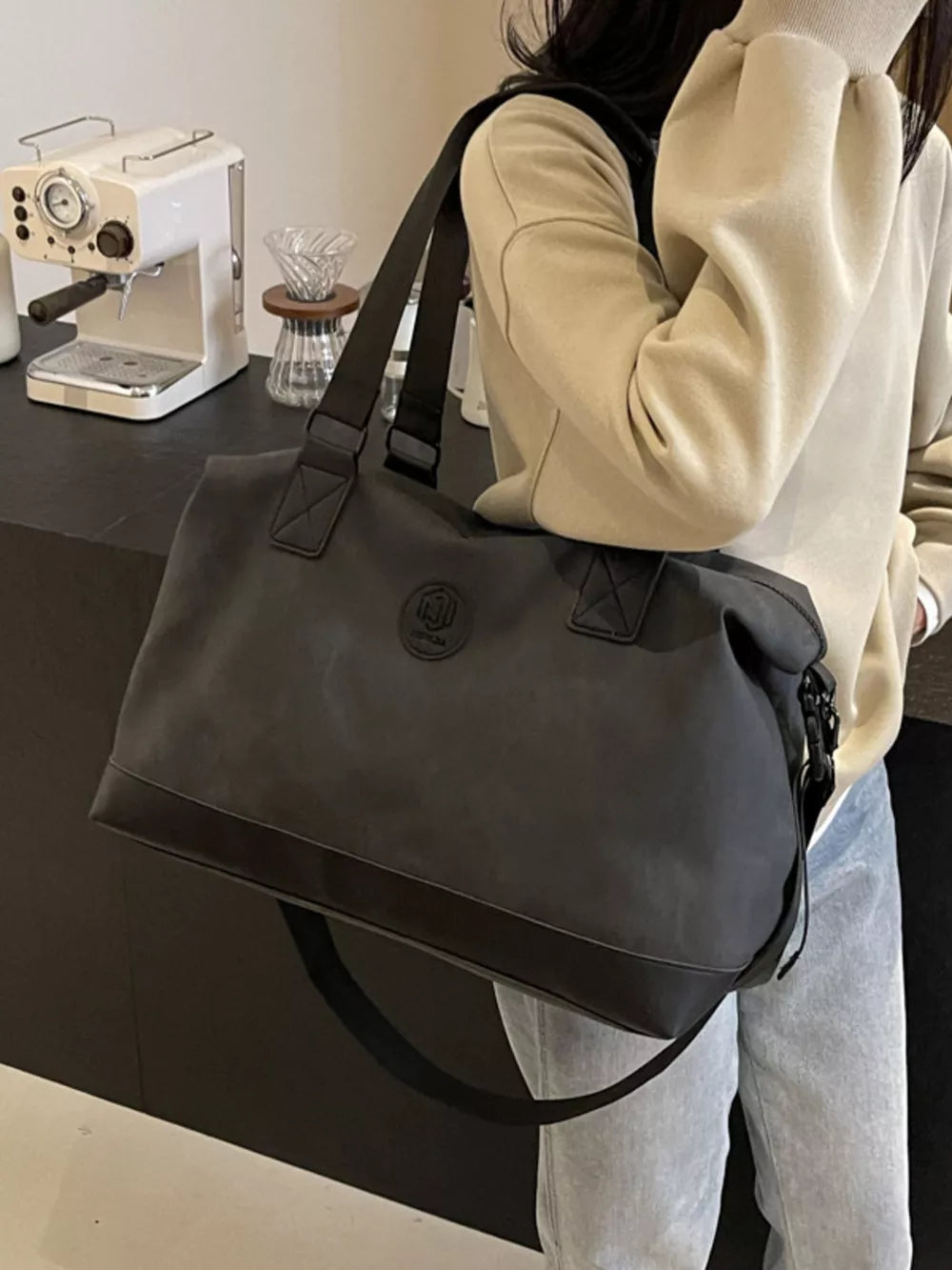 Black distressed duffle bag with adjustable strap and embossed logo detail.