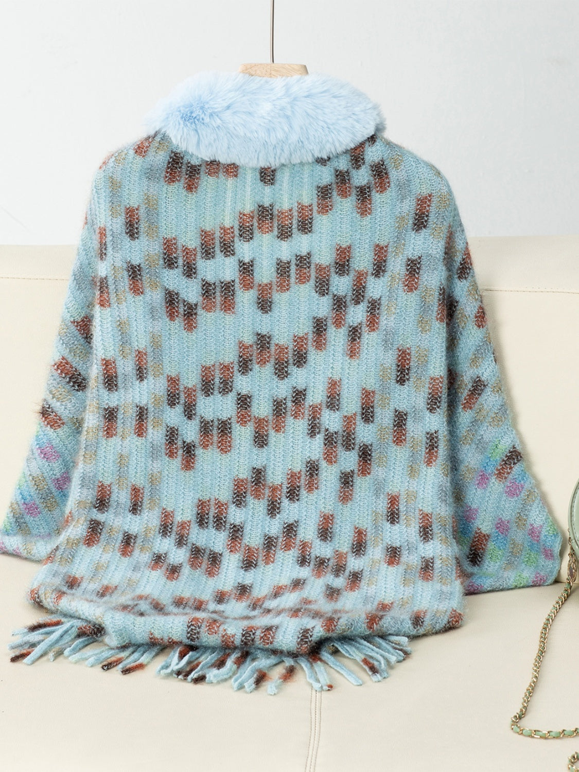 Pastel blue acrylic poncho with faux fur collar, geometric pattern, and fringe detail.