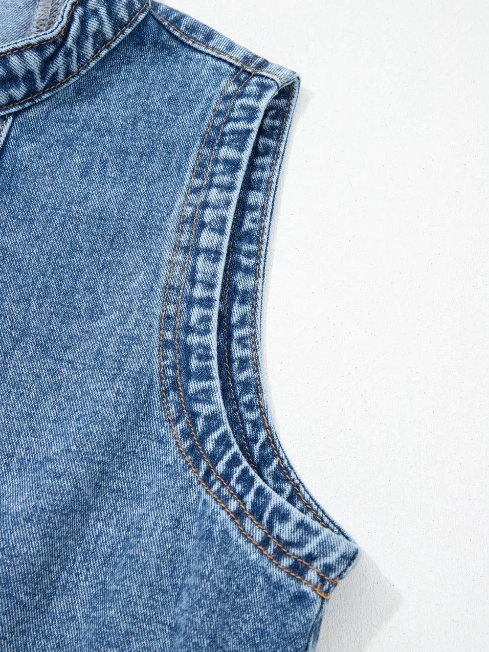 Belted denim dress detail showing contrast stitching on the sleeveless armhole and collar.