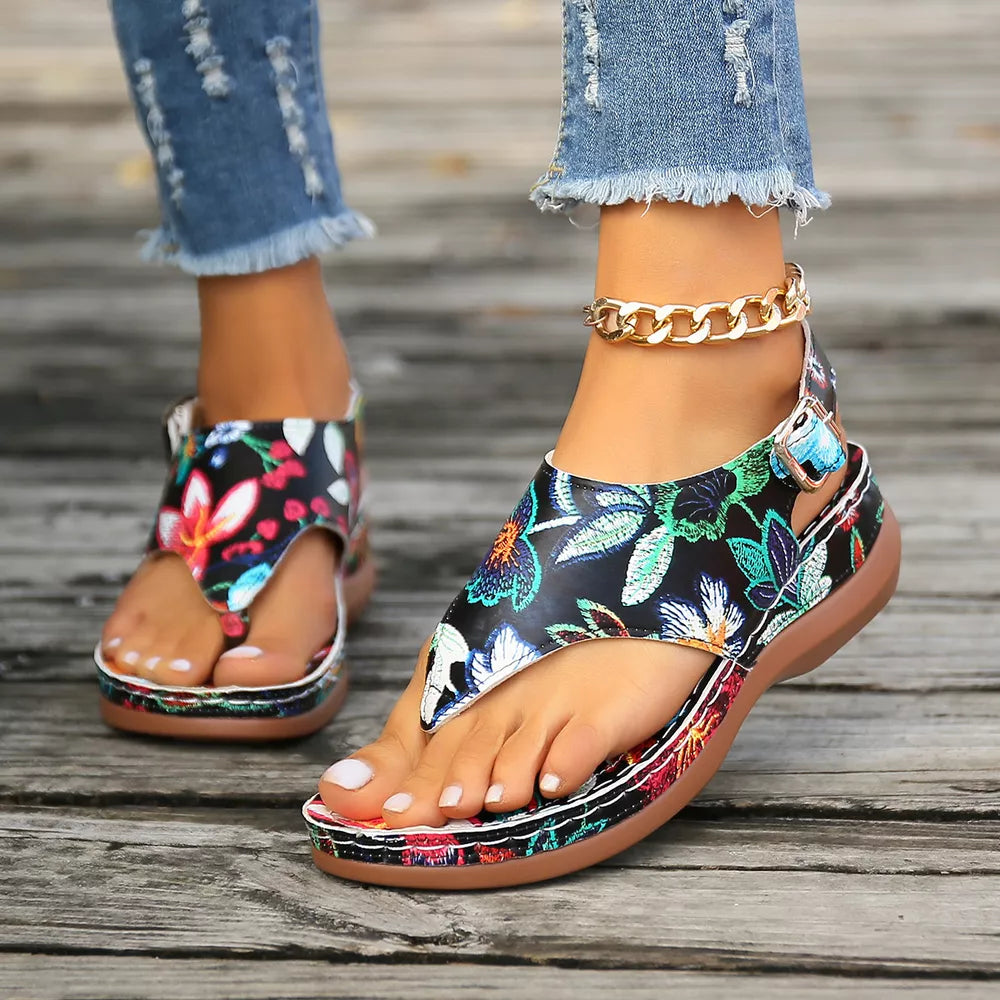 Embroidered floral thong wedge sandals with adjustable ankle strap and gold chain accent.