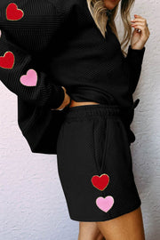 Black quilted lounge set with heart appliqués on sleeves and shorts.