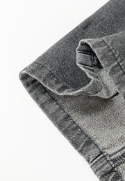 Faded gray denim pinafore dress detail showing hem and pocket construction.