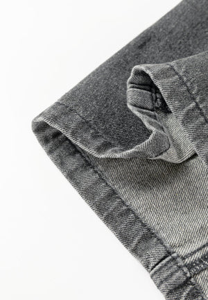 Faded gray denim pinafore dress detail showing hem and pocket construction.