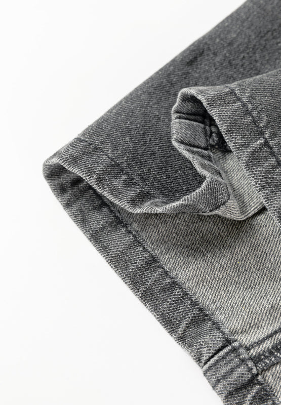 Faded gray denim pinafore dress detail showing hem and pocket construction.