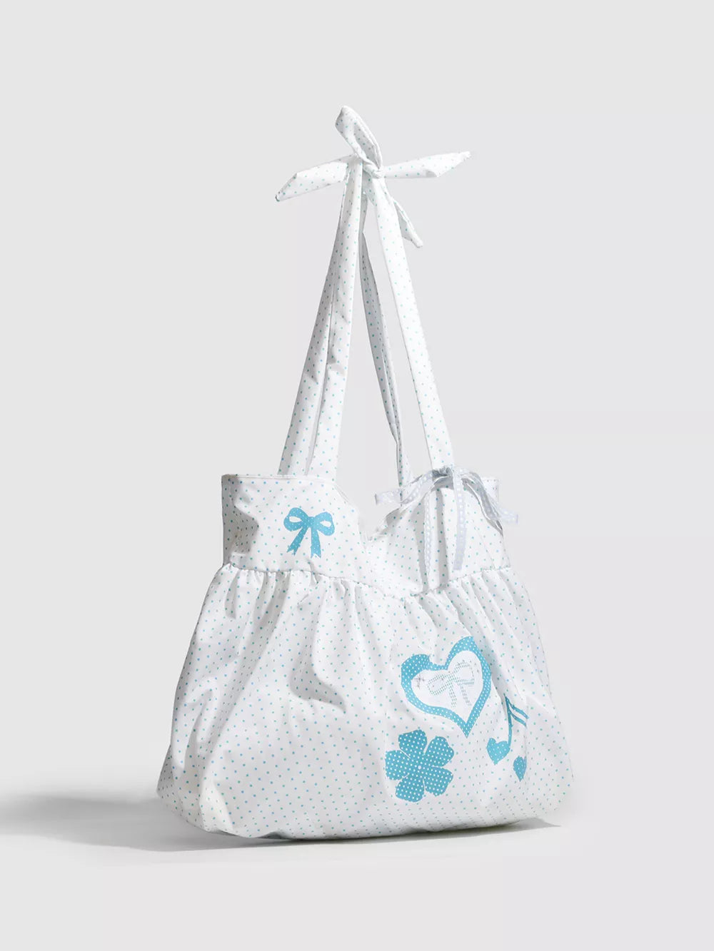 White polka dot canvas shoulder bag with blue heart appliqué and bow details.