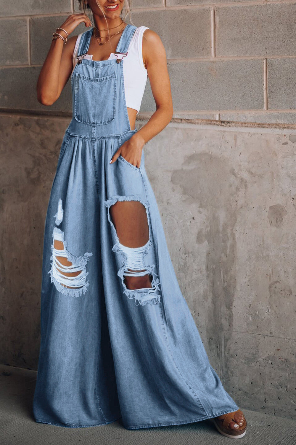 Distressed denim palazzo dungaree jumpsuit in light wash with ripped details and wide legs.