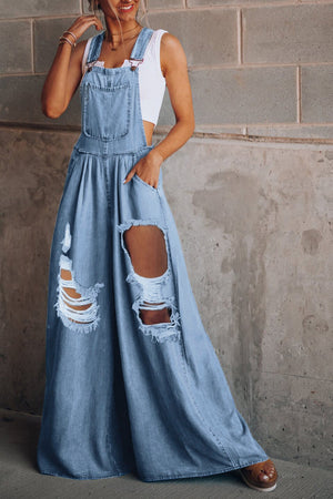 Distressed denim palazzo dungaree jumpsuit in light wash with ripped details and wide legs.