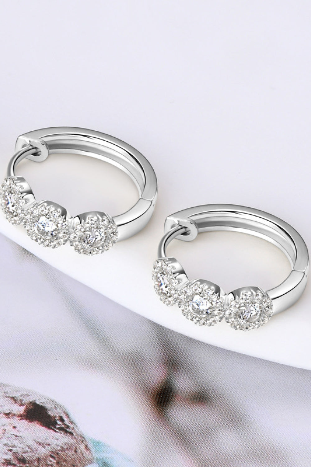 Silver triple cluster diamond huggie hoop earrings with three round cubic zirconia stones.