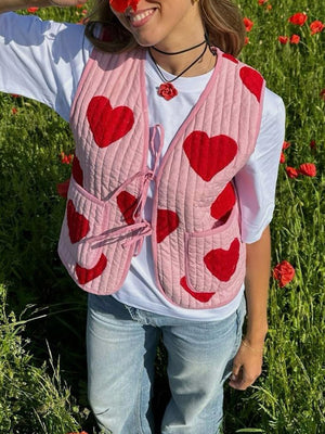 Quilted blush pink vest with red heart appliqué and tie closure, worn over a white tee.