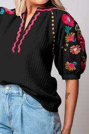 Black blouse with voluminous embroidered sleeves and pink neckline detail.