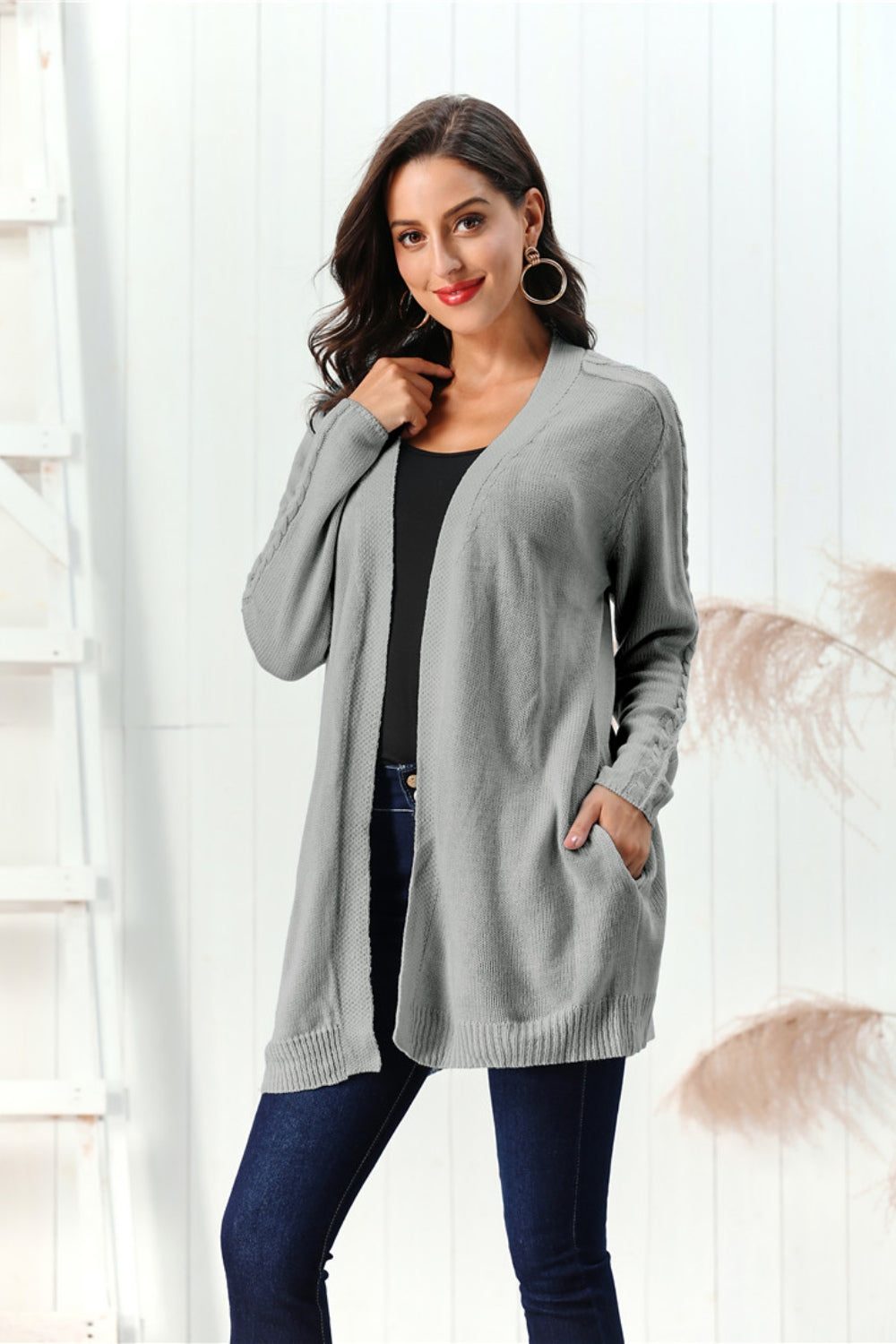Gray cable knit open front cardigan with pockets and braided sleeve detail.
