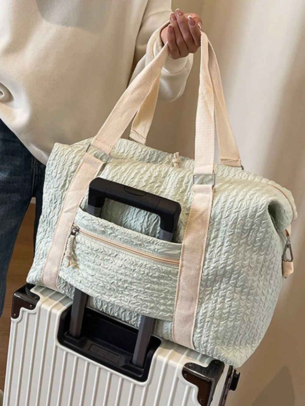 Textured travel bag with cream straps and front zip pocket, shown on a suitcase.