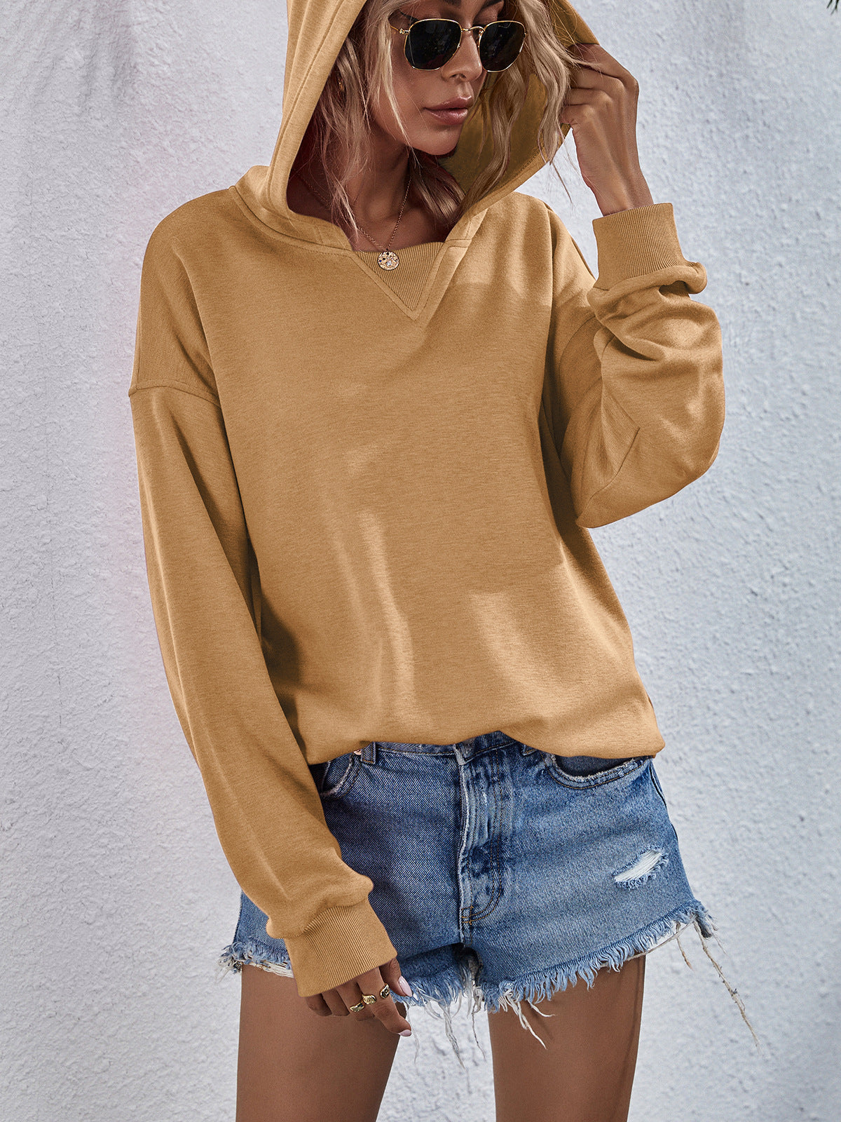 Tan boxy hooded sweatshirt with V-neck detail and split hem, styled with denim shorts.