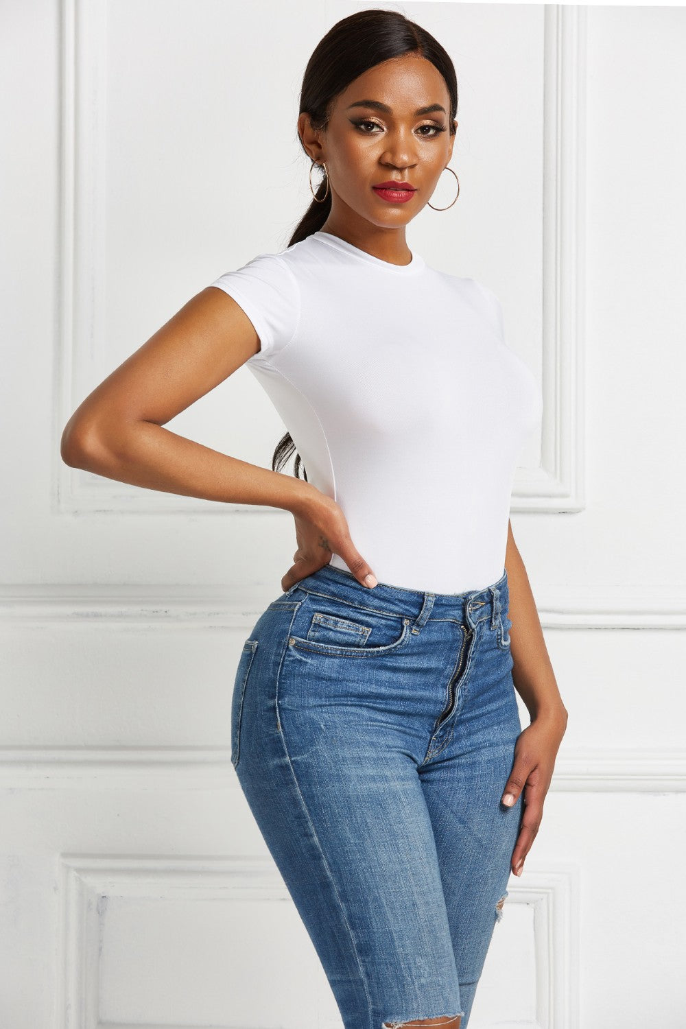 White crew neck short sleeve bodysuit with a sculpted fit, paired with blue denim jeans.