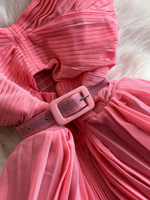Pink belted midi dress with spaghetti straps and pleated fabric detail.