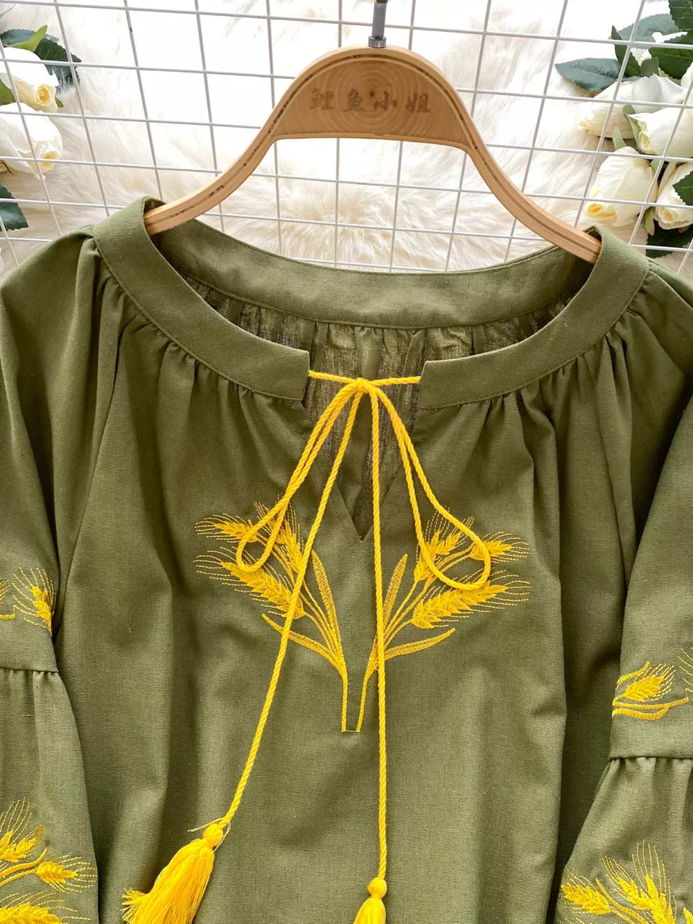 Green tie-neck blouse with yellow wheat embroidery and tassels.