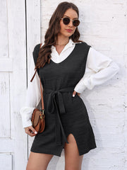 Black knit vest dress with V-neck, tie waist, and side slit, layered over a white shirt.