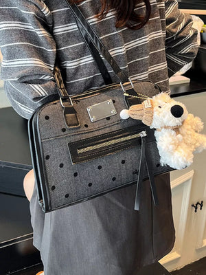 Sophisticated polka dot shoulder bag in black with a plush dog charm and zippered front pocket.