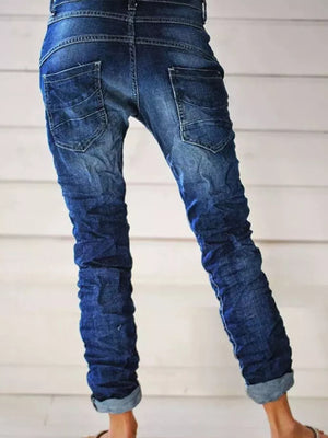 Dark blue cuffed button-fly jeans with ruched leg detail and distressed pockets.