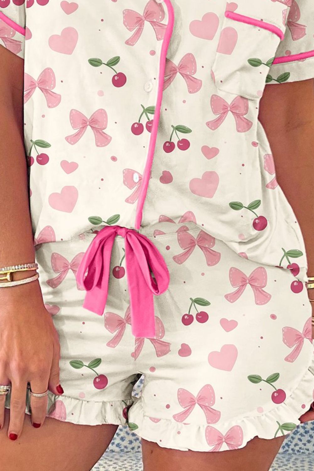Ivory pajama set with pink bows and cherries, featuring a button-up top and ruffled shorts.