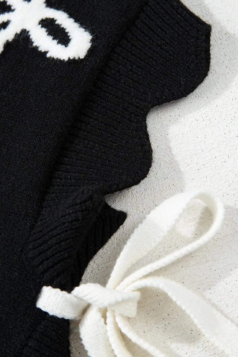 Black knit vest with white bow print and scalloped hem detail.